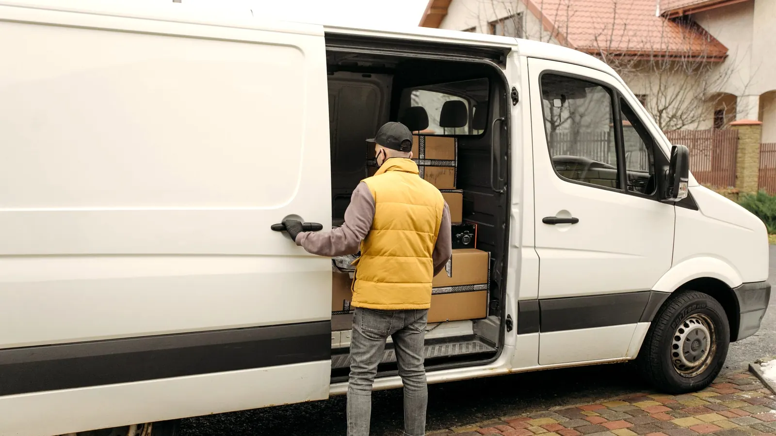 Worker loading boxes into a work van outside a home